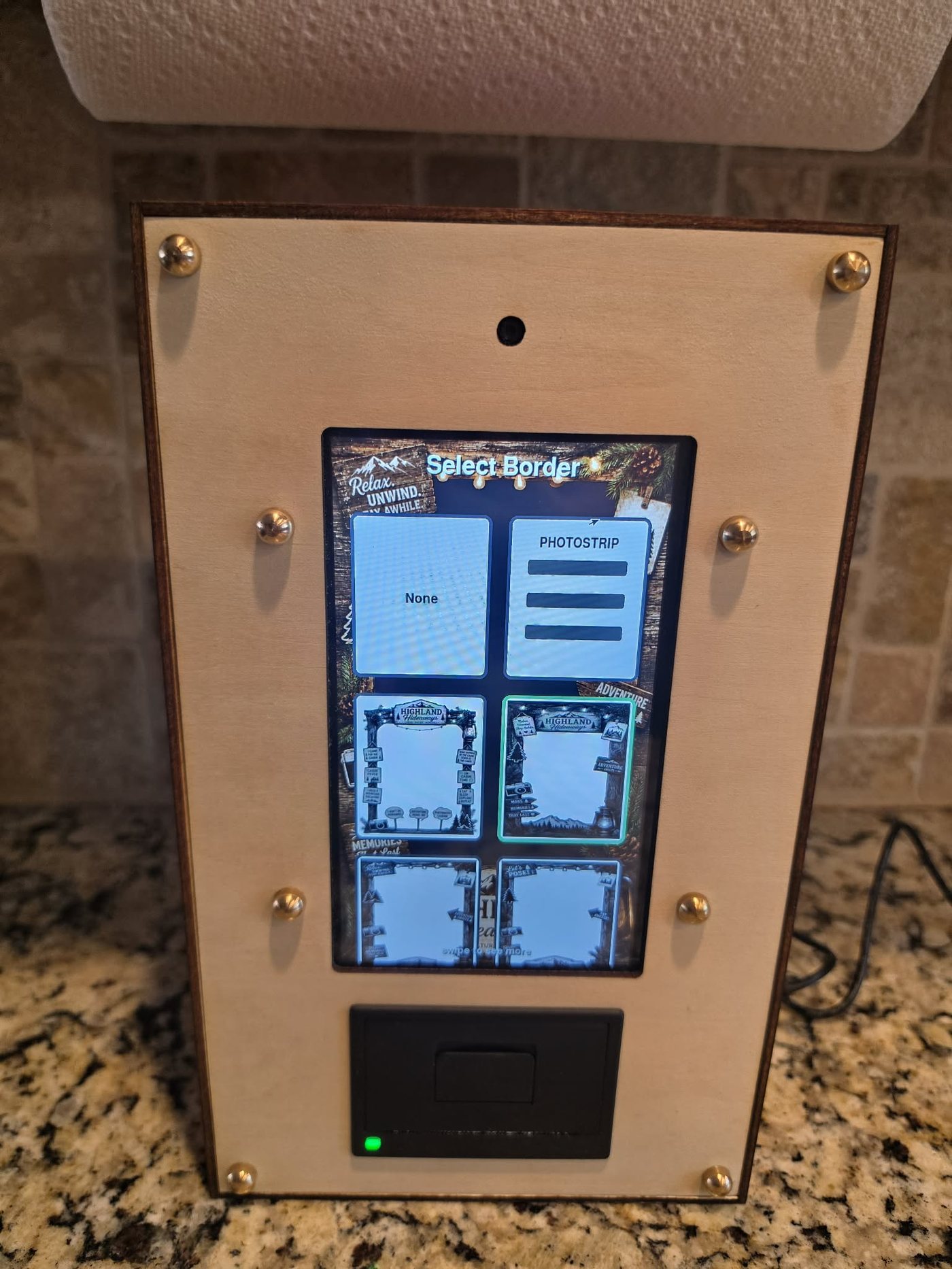 Paperbooth unit on a kitchen counter, showing the border-selection screen and paper feed slot
